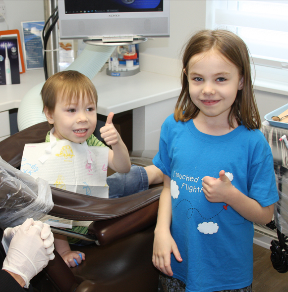 Two young children giving thumbs up during dental checkups and teeth cleanings for kids