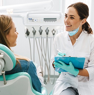 Smiling dentist talking to patient and taking notes on clipboard