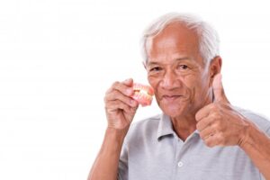 older man holding dentures and giving a thumbs up